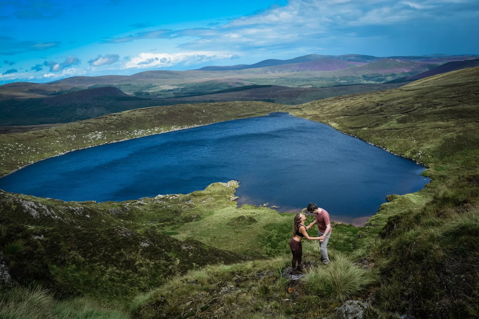 man in black shorts standing on cliff near lake during daytime